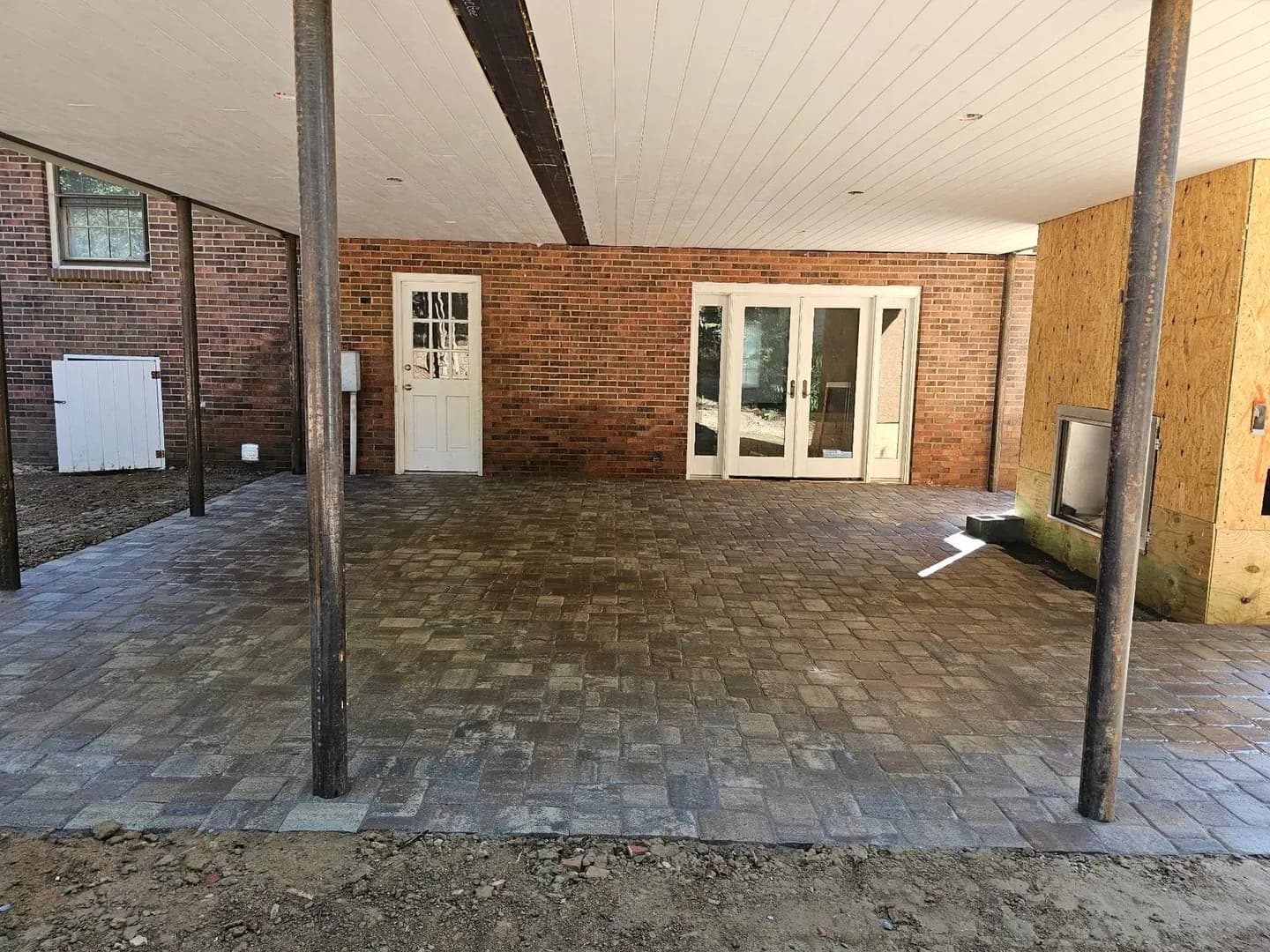 Covered Patio with Cobblestone Pavers by Alex's Lawnscape in Charlotte NC — Completed covered paver patio with cobblestone-style pavers, brick house facade, and French door access