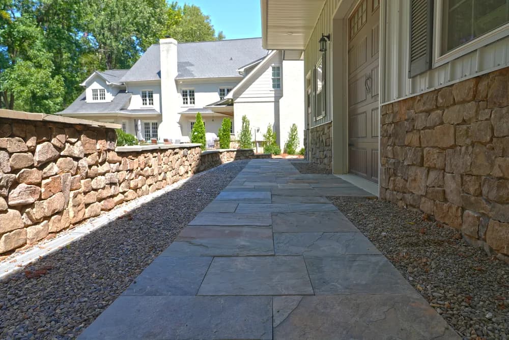 Bluestone Walkway & Stone Wall by Alex's Lawnscape in Charlotte NC — Elegant bluestone walkway flanked by natural stone retaining wall and river gravel between upscale buildings
