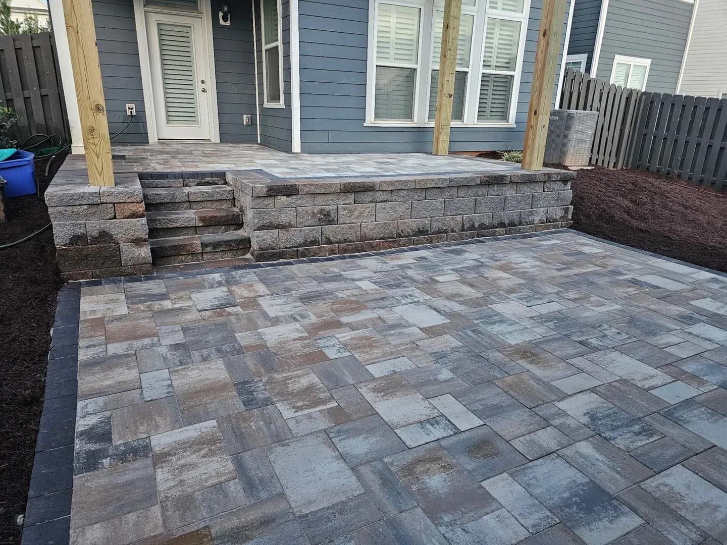Stepped Patio with Retaining Walls by Alex's Lawnscape in Charlotte NC — Two-tier paver patio connected by retaining wall block steps with dark border accent and fresh mulch landscape beds