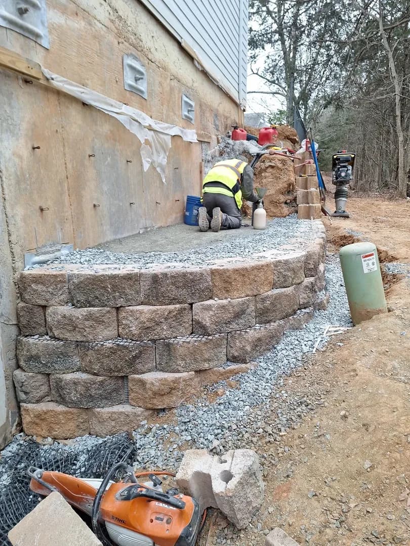 Terraced Patio with Lighting by Alex's Lawnscape in Charlotte NC — Wide shot of completed terraced retaining walls with integrated step lighting, paver patio, and steps leading up to a brick home with wood deck