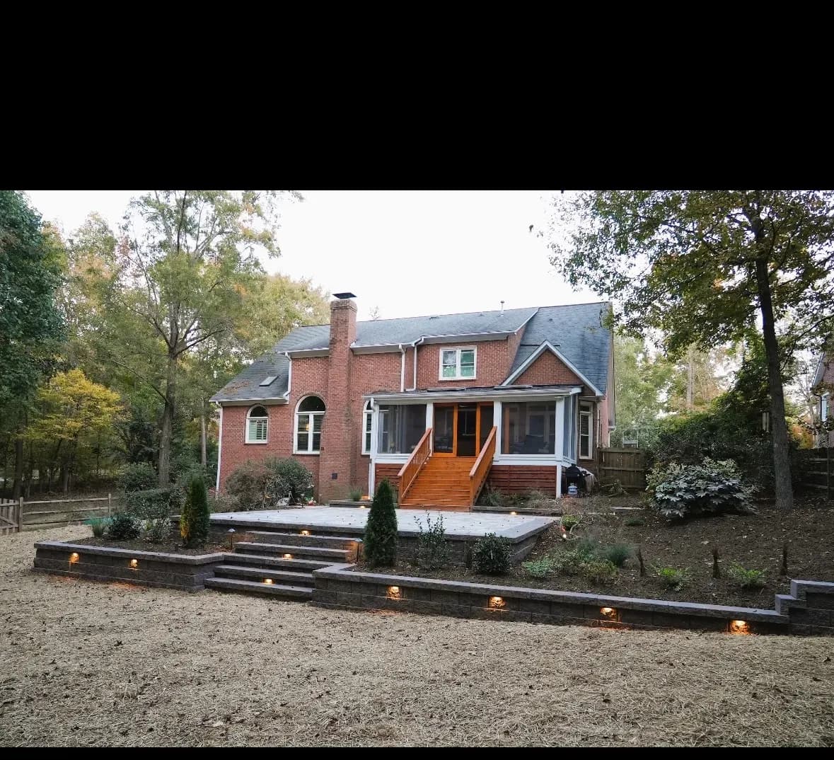 Complete Backyard Makeover by Alex's Lawnscape in Charlotte NC — Full backyard transformation — tiered retaining walls with integrated LED step lighting, raised paver patio, cedar deck with screened porch, and fresh plantings throughout